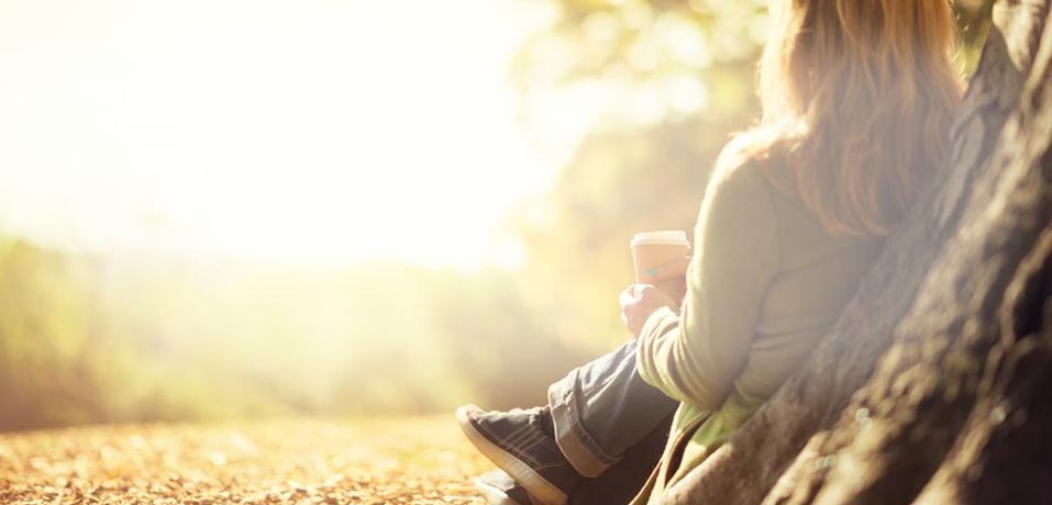 A woman sitting against a tree holding a coffee