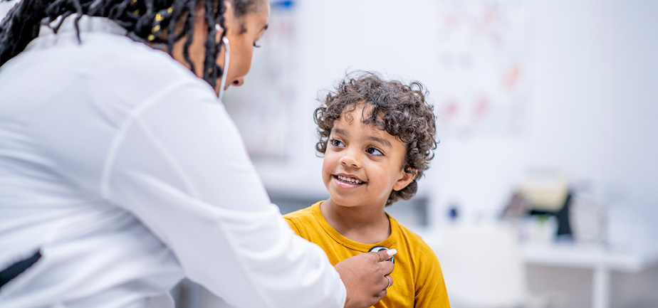 A five year old boy of mixed race ethnicity is sitting on the examination table and looking at his doctor while he is getting his heart rate checked.