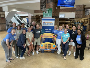 Essentia volunteers gathered around a large school bus-shaped sign